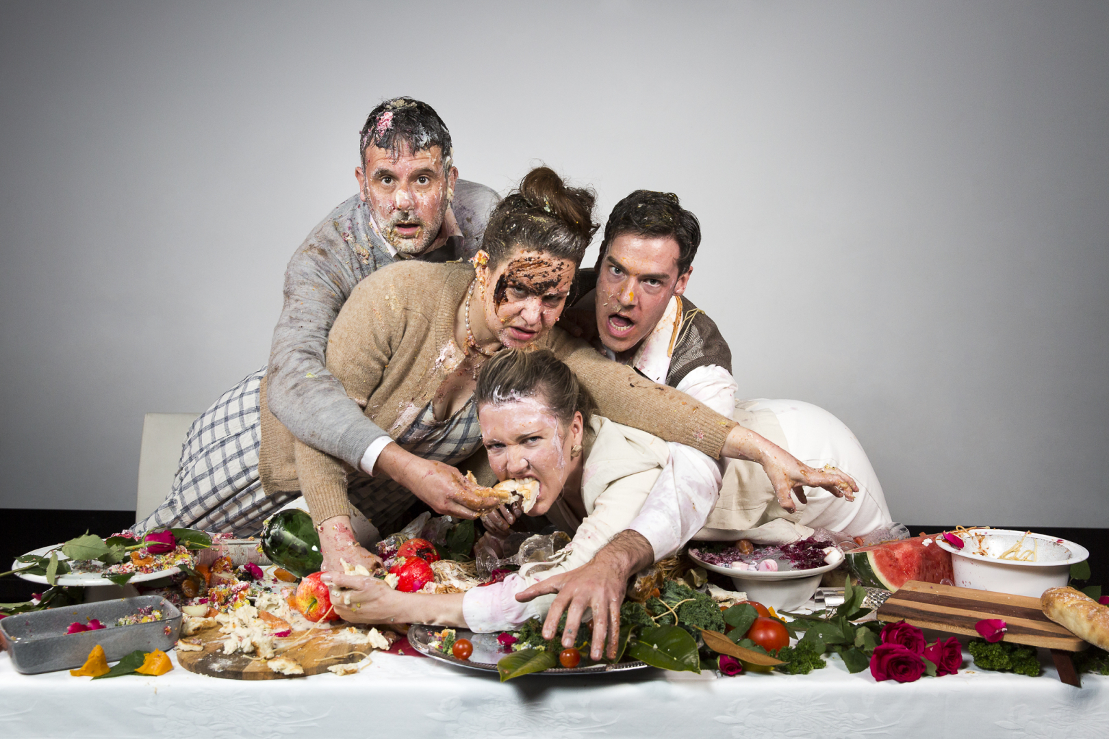 Two couples covered in food after a fight scrabble around on a table laden with more food. 