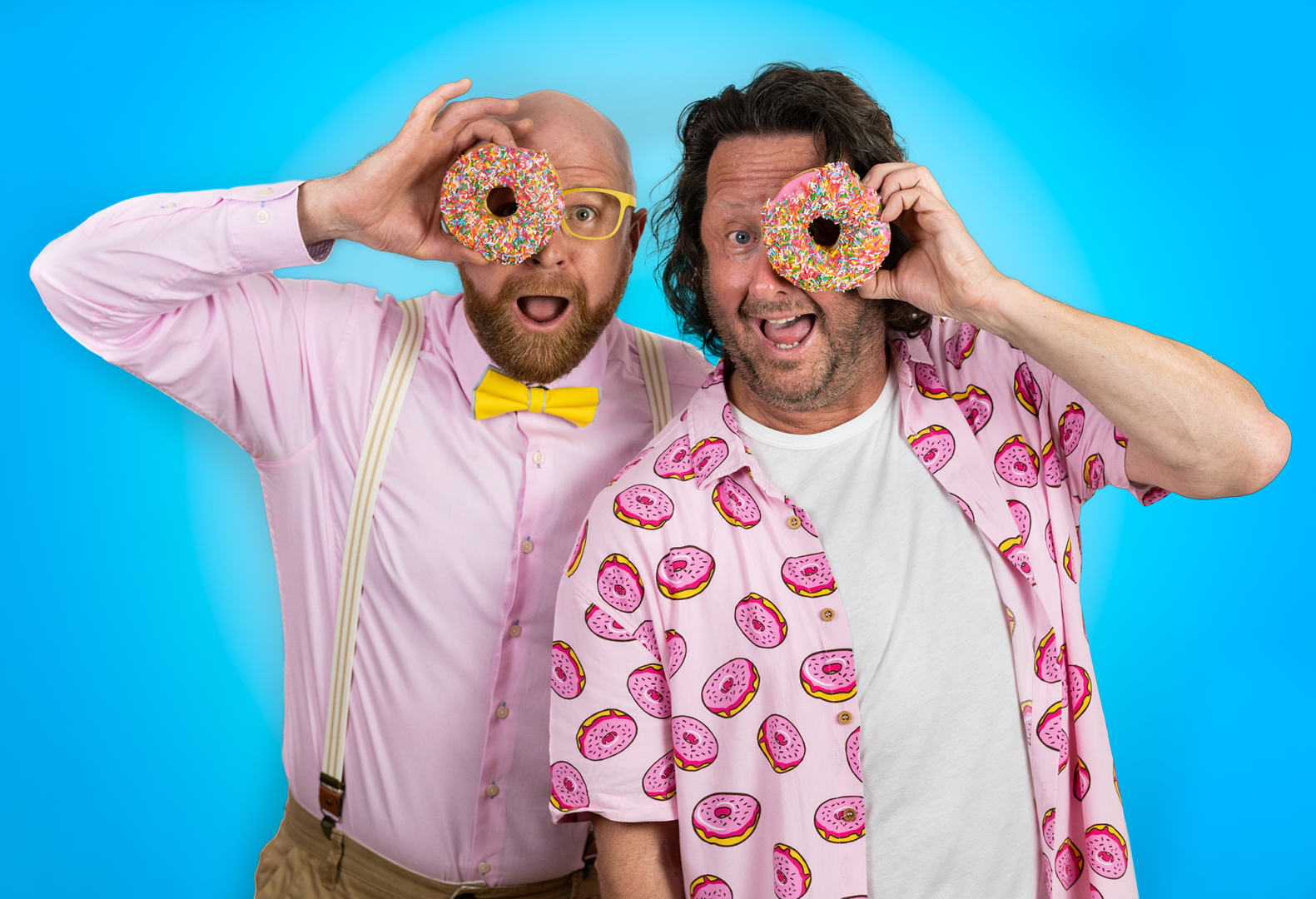 Two men smile with pink frosted donuts