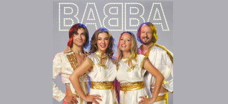 Image of the four band members of BABBA - two women and two men dressed in the typical ABBA costume - white spandex style dress with bright gold trim. They smile enthusiastically at the camera! 