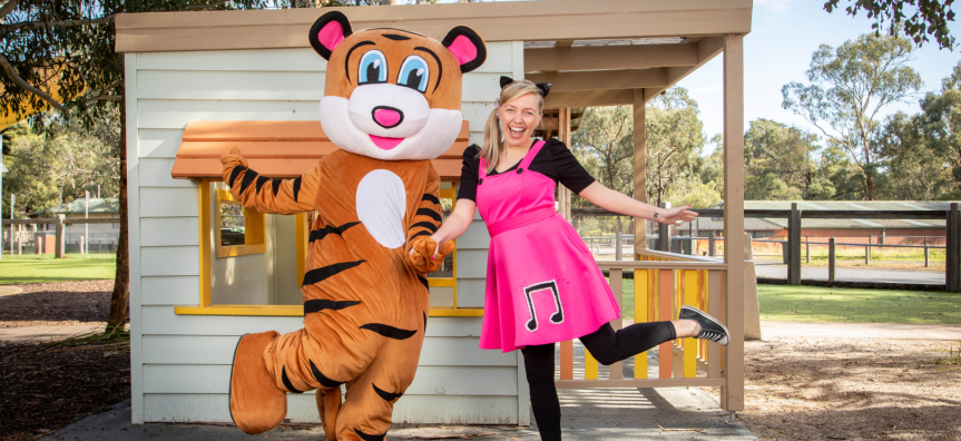 A large tiger stands next to their friend, a woman with blonde hair in pigtails smiling!