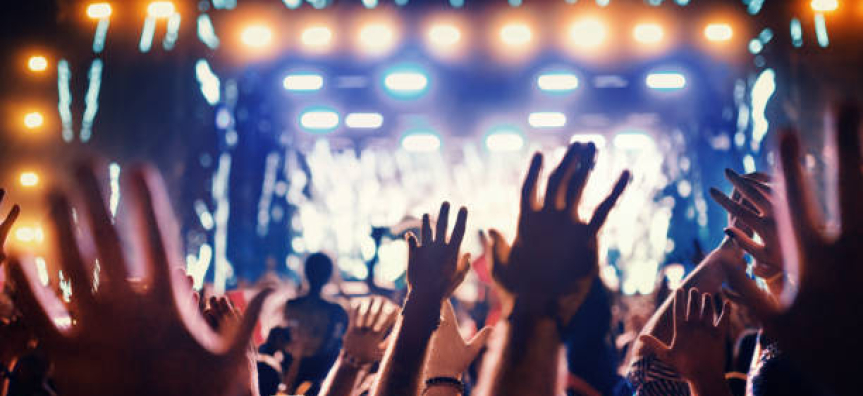 Many hands reach into the air in front of a large stage with lights