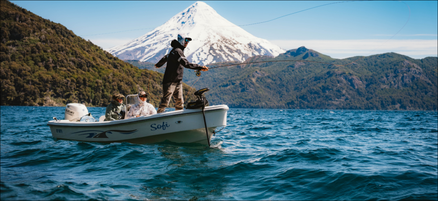 Fly fisher casting in beautiful blue waters with a snowy mountain in the background