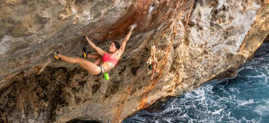 A female rock climber ascending a steep cliff above ocean.