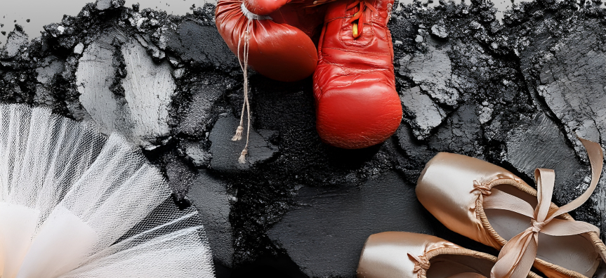 Red boxing gloves, a pink tutu and pink ballet shoes are splayed on a grey background. 